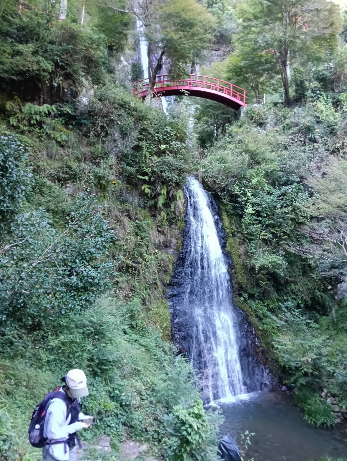 赤い橋を渡る妻と、そのすぐそばに流れる滝